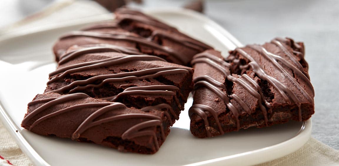 On a rectangular plate, there are three Fibre 1 Brownie bars, Chocolatey Fudge Flavour.